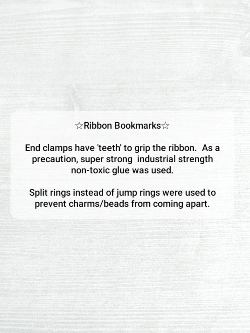 May include: A white card with black text describing the features of ribbon bookmarks. The text reads: "Ribbon Bookmarks. End clamps have 'teeth' to grip the ribbon. As a precaution, super strong industrial strength non-toxic glue was used. Split rings instead of jump rings were used to prevent charms/beads from coming apart."