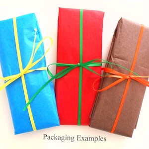 May include: Three gift boxes wrapped in different colors of tissue paper with matching ribbon. The boxes are blue, red, and brown. The blue box has yellow ribbon, the red box has green ribbon, and the brown box has orange ribbon. The text "Packaging Examples" is printed below the boxes.