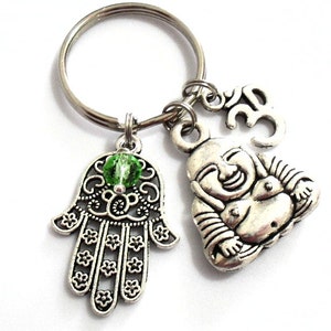 May include: Silver charm keychain with a green crystal, a hamsa hand charm, a laughing Buddha charm, and an Om symbol charm.