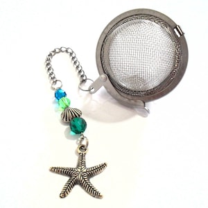 May include: A silver tea infuser with a mesh ball and a chain attached to a starfish charm. The chain is decorated with green and blue beads.