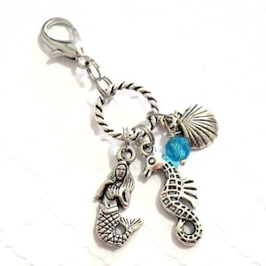 Peut inclure: Charm argenté avec une sirène, un hippocampe et un coquillage. Une perle bleue orne le charme de l'hippocampe. Les breloques sont fixées à un fermoir argenté et à un anneau torsadé.