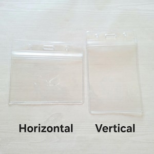 Puede incluir: Dos porta-credenciales de plástico transparente, uno horizontal y otro vertical, se muestran sobre un fondo claro con vetas de madera. El porta-credenciales horizontal es rectangular, mientras que el vertical es más alto y estrecho. El texto debajo dice "Horizontal" y "Vertical".