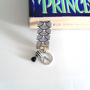 May include: A black and white patterned bookmark with a silver charm and black and white beads. The bookmark is hanging from a book with the word "Princess" on the cover.