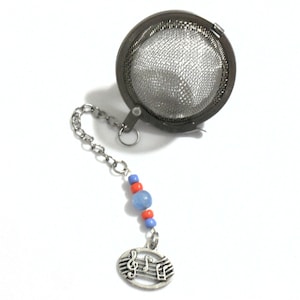 May include: A stainless steel tea infuser with a chain and decorative beads. The chain is attached to a round mesh basket and a charm with musical notes. The beads are blue and orange.