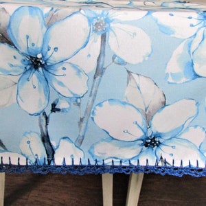 以下が含まれることがあります： 青い花柄のテーブルランナーで、縁はクロシェ編みです。ランナーは、薄い青色の背景に、水彩画風の青い花と白い花が描かれています。