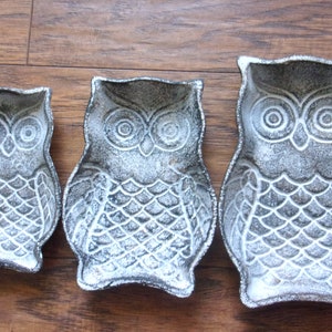 May include: Three white ceramic owl-shaped dishes of varying sizes. The owls have a distressed white finish with black detailing.