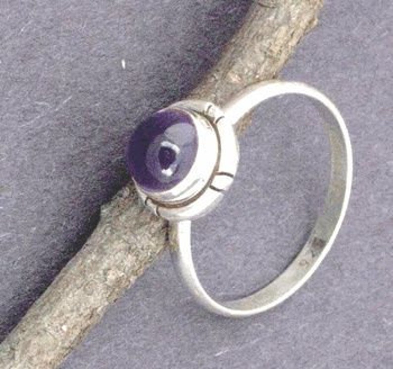 May include: A silver ring with a purple amethyst gemstone set in a bezel setting. The ring has a simple band and a delicate design.