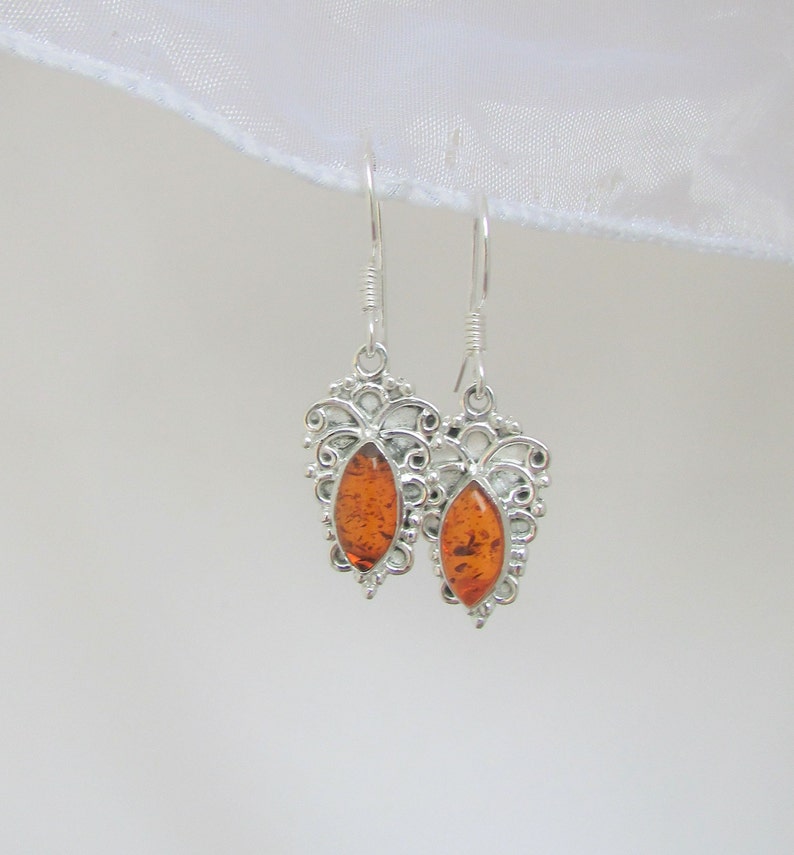 Handmade of natural Baltic Amber and sterling silver.  Fine silver work with amazing details around the gems.
Measures Approx. 1in L x  1/2in W.
 they drop 1.52 inches