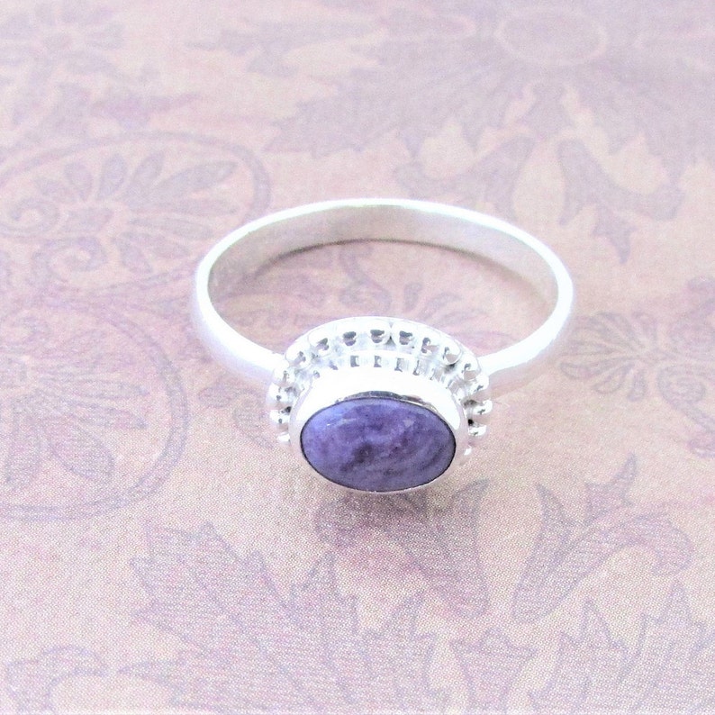 May include: A silver ring with a purple gemstone set in a beaded bezel.