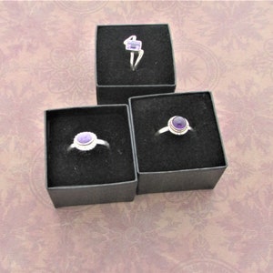May include: Three small black ring boxes with purple amethyst rings inside. The rings are set in silver.