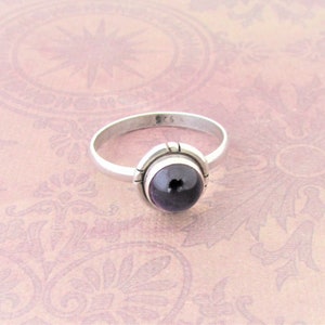 May include: A silver ring with a dark purple gemstone set in a bezel setting. The ring is marked "925" on the inside band.