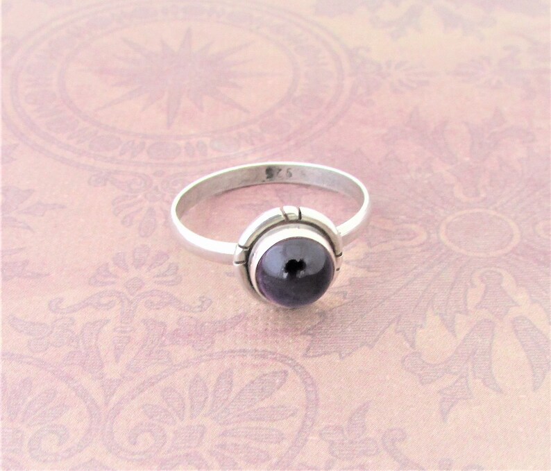 May include: A silver ring with a dark purple gemstone set in a bezel setting. The ring is marked "925" on the inside band.