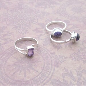 May include: Two silver rings with purple amethyst gemstones. One ring has a round stone and the other has a rectangular stone.