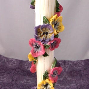 May include: A cream-coloured decorative pillar decorated with colourful pansy flowers in shades of pink, yellow, and purple. The pillar has a square base and a decorative top.