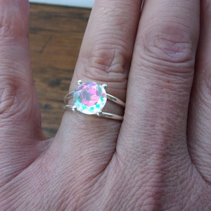 May include: A silver ring with a large, iridescent gemstone. The gemstone is a round, faceted cut and has a pink, blue, and green color.