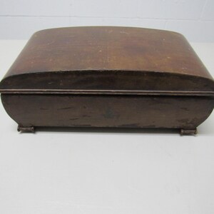 Puede incluir: Una caja de madera vintage con tapa curvada y acabado marr&oacute;n oscuro. La caja tiene forma rectangular con bordes redondeados y se apoya sobre peque&ntilde;os pies. La caja probablemente se utiliza para el almacenamiento.