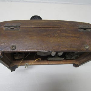 Puede incluir: Una caja de madera vintage con tapa con bisagras y herrajes met&aacute;licos. La caja tiene un acabado marr&oacute;n oscuro y parece ser antigua. Los componentes internos son visibles, lo que sugiere que podr&iacute;a ser una radio o un dispositivo similar.