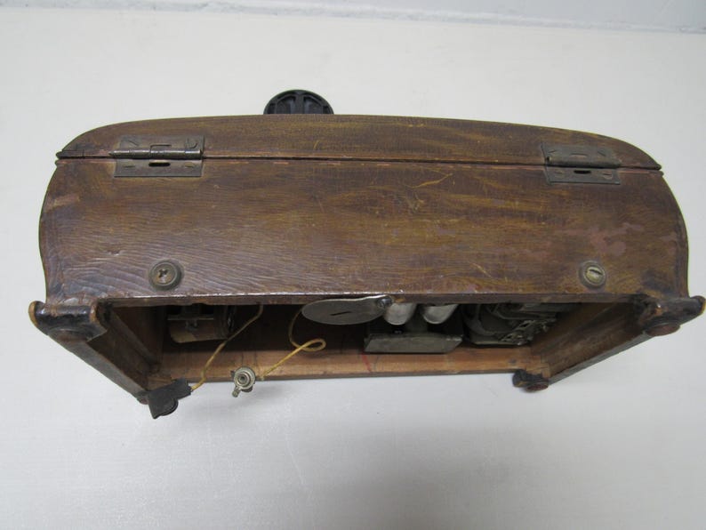 Puede incluir: Una caja de madera vintage con tapa con bisagras y herrajes met&aacute;licos. La caja tiene un acabado marr&oacute;n oscuro y parece ser antigua. Los componentes internos son visibles, lo que sugiere que podr&iacute;a ser una radio o un dispositivo similar.