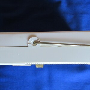 May include: A cream-coloured rectangular object with a metal rod extending from the top. The object has a small, rectangular opening on the bottom and a series of small ridges along one side. The background is a solid blue.