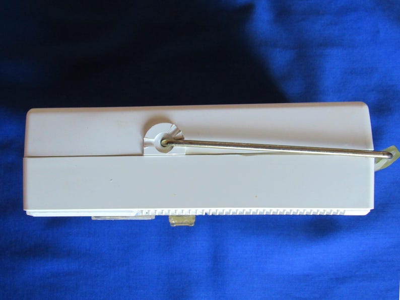 May include: A cream-coloured rectangular object with a metal rod extending from the top. The object has a small, rectangular opening on the bottom and a series of small ridges along one side. The background is a solid blue.