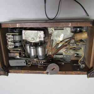 Puede incluir: Se ven los componentes internos de una radio antigua, que muestran v&aacute;lvulas de vac&iacute;o, cableado y un condensador de sintonizaci&oacute;n dentro de un marco de madera. El interior de la radio es una compleja disposici&oacute;n de piezas electr&oacute;nicas.