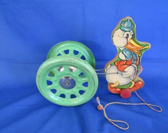 May include: A vintage pull toy featuring a cartoon duck with a green metal wheel and a red wheel. The duck is painted white with red, orange, and blue details. The toy has a string attached to the duck's tail.