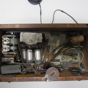 Puede incluir: Los componentes internos de una radio antigua son visibles dentro de un marco de madera. El interior presenta v&aacute;lvulas de vac&iacute;o, condensadores y cableado, mostrando la intrincada tecnolog&iacute;a del dise&ntilde;o de radio antiguo. El marco de madera tiene herrajes envejecidos.