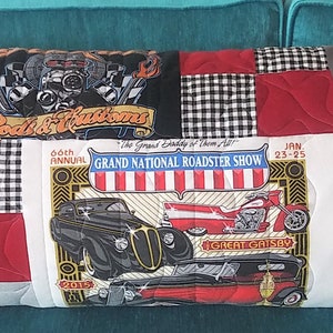 May include: A patchwork pillow with a variety of car-themed designs. The pillow is made from different fabrics, including black and white checkered, red, and yellow. The pillow features images of classic cars, including a red hot rod, a black and white checkered car, and a yellow car with a red stripe. The pillow also features the text "Spectator", "Salina Kansas", "Grand National Roadster Show", and "Roadsters".