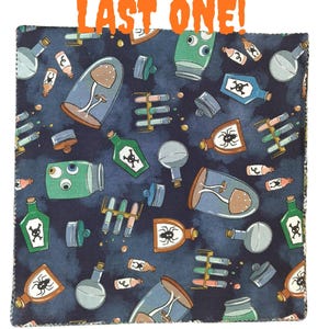 May include: A square fabric swatch with a dark blue background featuring a repeating pattern of potion bottles, test tubes, mushrooms in glass domes, and jars with eyeballs and spiders. The text LAST ONE! is printed in orange at the top.