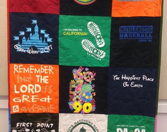 Può includere: Una trapunta realizzata con diverse magliette con diversi disegni e testi. La trapunta è composta da 9 quadrati. Il quadrato in alto a sinistra è rosso con il testo "ARCADIA UNIVERSITY". Il quadrato in alto al centro è nero con un cerchio rosa neon con il testo "Greeks through the Decades". Il quadrato in alto a destra è arancione con il testo "SURF SHACK vbs 2016". Il quadrato in basso a sinistra è blu scuro con un castello blu e il testo "Greek Week 2017". Il quadrato in basso al centro è verde con un'impronta bianca e il testo "I'M WALKING TO CALIFORNIA! 5.6 MILLION". Il quadrato in basso a destra è blu scuro con il testo "MUHLENBERG BASEBALL 2012 DL". Il quadrato in basso a sinistra è arancione con il testo "REMEMBER that THE LORD is GREAT & AWESOME". Il quadrato in basso al centro è bianco con una grafica multicolore degli anni '60, '70, '80 e '90. Il quadrato in basso a destra è blu scuro con il testo "The Happiest Place On Earth".