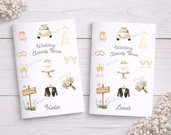 May include: Two white wedding activity books featuring watercolour illustrations of a car, dress, rings, champagne, cake, doves, sign, suit, and bouquet. The text Wedding Activity Book is printed on both, with the names Katie and Lewis at the bottom.
