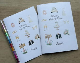 Puede incluir: Dos libros de actividades de boda blancos con ilustraciones en acuarela de un coche, vestido, anillos, champán, pastel, palomas, ramo, esmoquin y un letrero. Los libros muestran el texto Wedding Activity Book y los nombres Katie y Lewis.