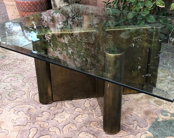 May include: A glass-top coffee table with a brass base. The table has a square shape and sits on a patterned rug.