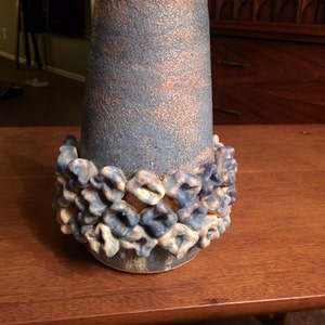 May include: A blue and white ceramic vase with a textured surface and a decorative band of white and blue flowers around the base.