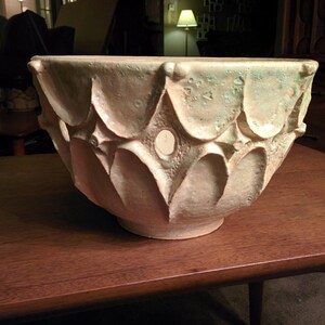 May include: A large, white ceramic bowl with a textured, geometric design. The bowl has a slightly green tint and is decorated with small, raised dots.
