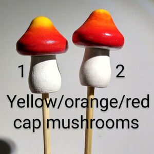 K&ouml;nnte beinhalten: Zwei Miniatur-Pilzfiguren mit Holzstielen. Die Pilzkappen sind in Gelb, Orange und Rot bemalt. Die Pilzstiehle sind wei&szlig;. Die Zahlen 1 und 2 sind auf dem Bild geschrieben.