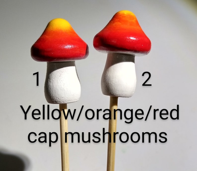 K&ouml;nnte beinhalten: Zwei Miniatur-Pilzfiguren mit Holzstielen. Die Pilzkappen sind in Gelb, Orange und Rot bemalt. Die Pilzstiehle sind wei&szlig;. Die Zahlen 1 und 2 sind auf dem Bild geschrieben.