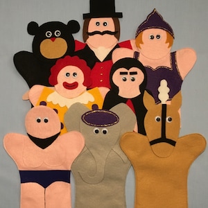 May include: A set of felt hand puppets featuring a ringmaster, a clown, a strongman, an elephant, a horse, a gorilla, a bear, and a woman in a purple dress. The puppets are all brightly colored and have googly eyes.