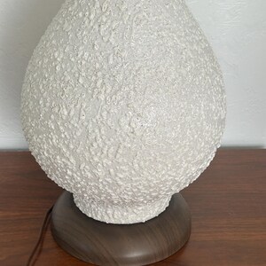 May include: White ceramic table lamp with a textured, bubble-like surface. The lamp has a dark wood base.