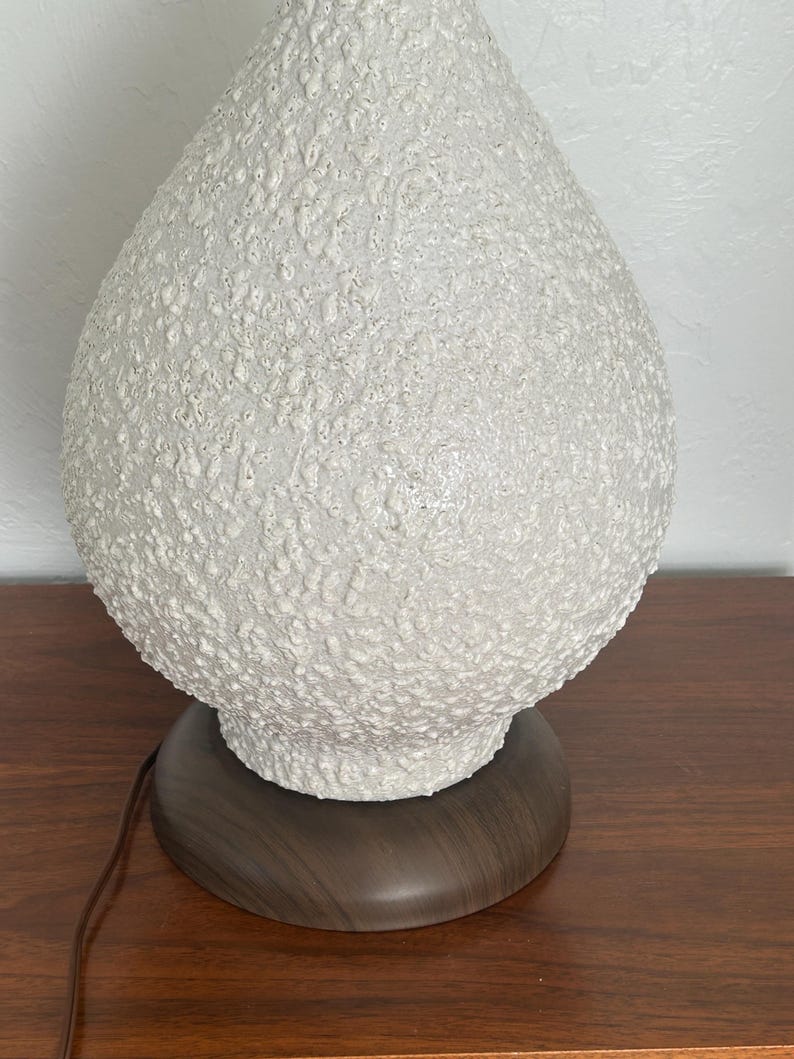 May include: White ceramic table lamp with a textured, bubble-like surface. The lamp has a dark wood base.