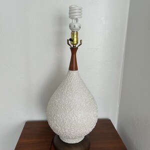May include: A white ceramic table lamp with a textured surface and a brown wooden base. The lamp has a white, spiral-shaped light bulb.