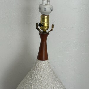May include: A white ceramic table lamp with a textured surface. The lamp has a wooden base and a white cord.