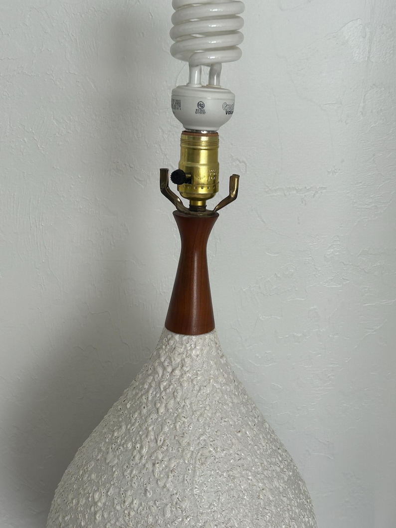 May include: A white ceramic table lamp with a textured surface. The lamp has a wooden base and a white cord.