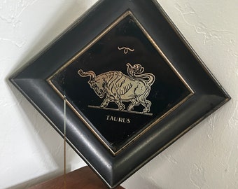 May include: A black framed square incense holder with a gold bull design and the word "TAURUS" printed below.