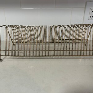 May include: A gold metal record rack with a grid design. The rack is empty and has a slight curve to it.