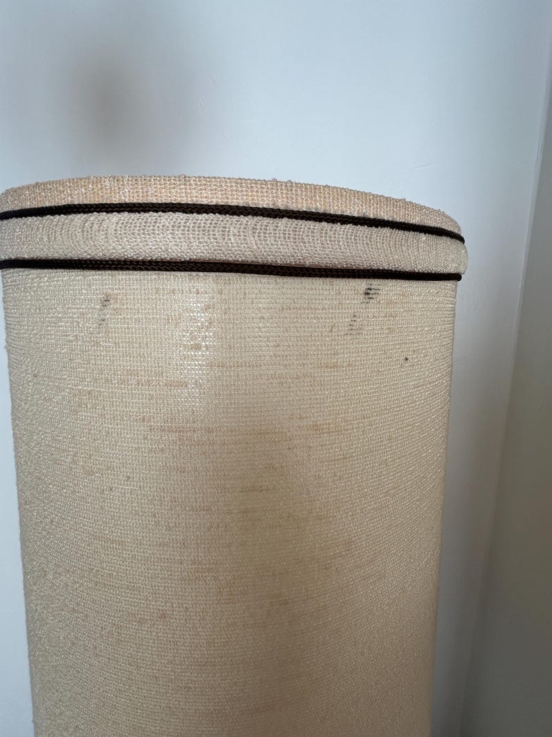 May include: A beige lampshade with a brown trim around the top.