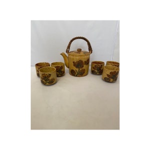 May include: A brown and tan ceramic teapot with a floral design and a woven handle, along with six matching teacups.