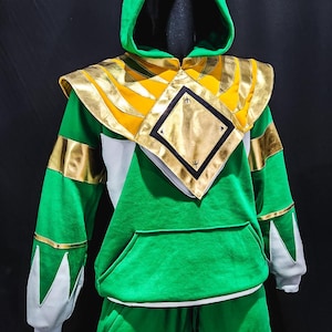 The MMPR Green Hoodie features a bold green fleece body combined with premium vegan leather accents, offering a battle-ready look inspired by the iconic Mighty Morphin Power Rangers. Designed for collectors and cosplayers, this hoodie merges classic hero aesthetics with modern comfort.