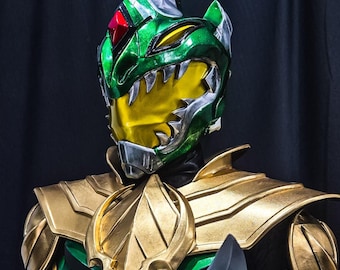May include: A green and gold helmet with a sharp, toothy mouth and a red jewel on the forehead. The helmet is part of a costume.