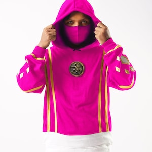 May include: A pink hoodie with gold accents and a gold emblem on the front. The hoodie has a hood and a face mask.